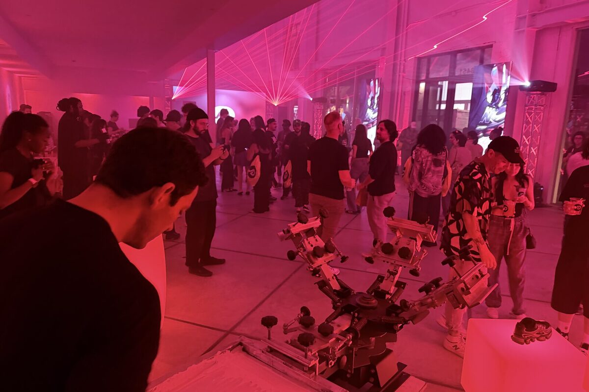 A screen-printing press running at a pink-lit nightlife brand activation with a crowd gathered around