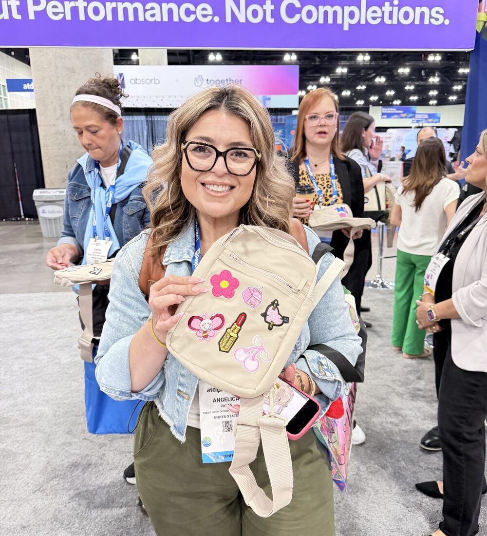 A smiling trade-show guest holds up a custom crossbody bag personalized with embroidered patches