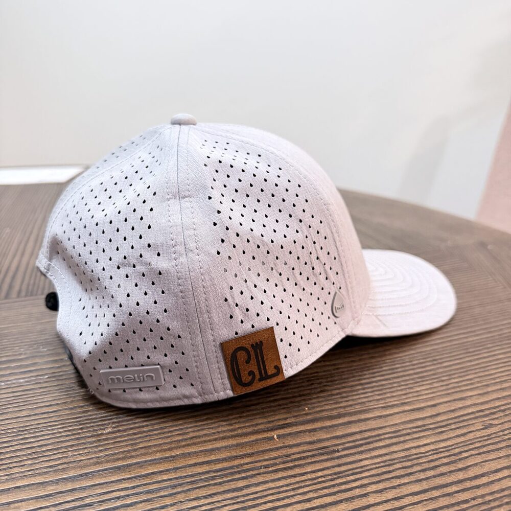 A custom light-gray cap with a leather monogram patch, made at a live hat bar